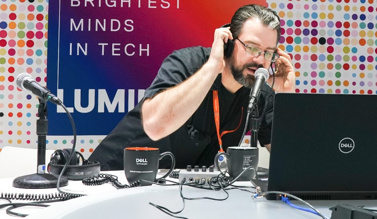 A man with headphones in front of a laptop speaking into a microphone.
