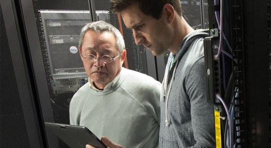 Two men stand in a Dell data center looking at database administration software on a Dell tablet