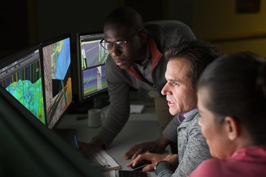  Three men look at diagrams on multiple computer monitors