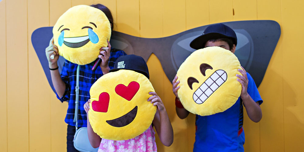 three children hold emoji pillows in front of their faces
