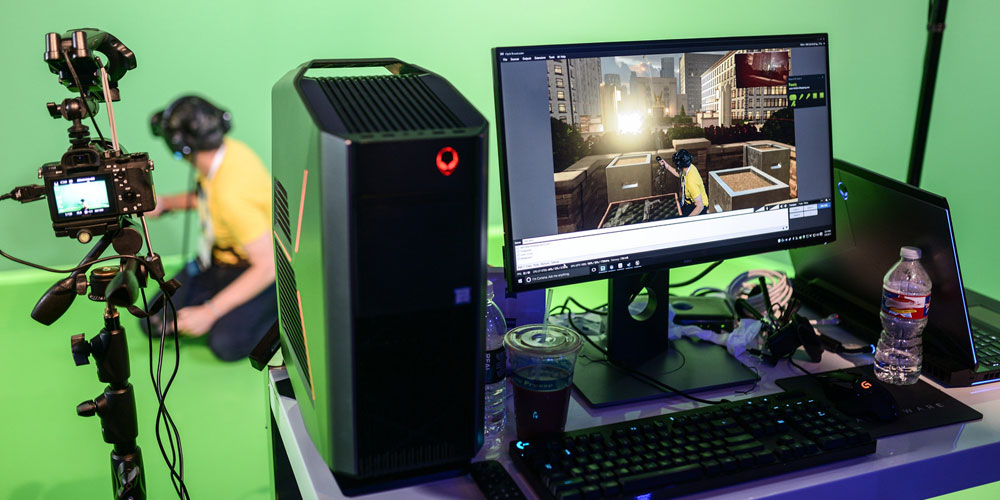 man in vr headset in front of green screen and alienware desktop laptop and dell monitor