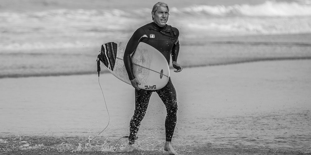 man running up beach holding a surf board