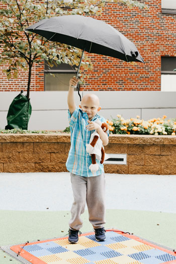 child standing with umbrella and stuffed toy
