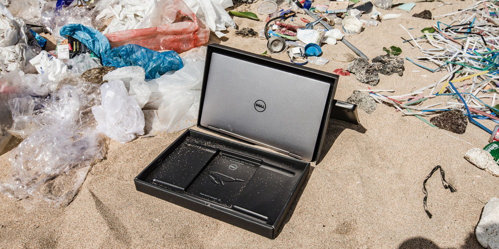 Dell laptop packaging on beach surrounded by ocean plastics that are recycled to create it