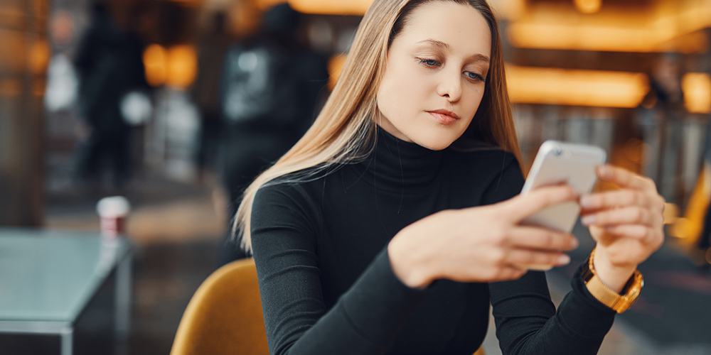 woman sitting at a cafe looking at her smartphone