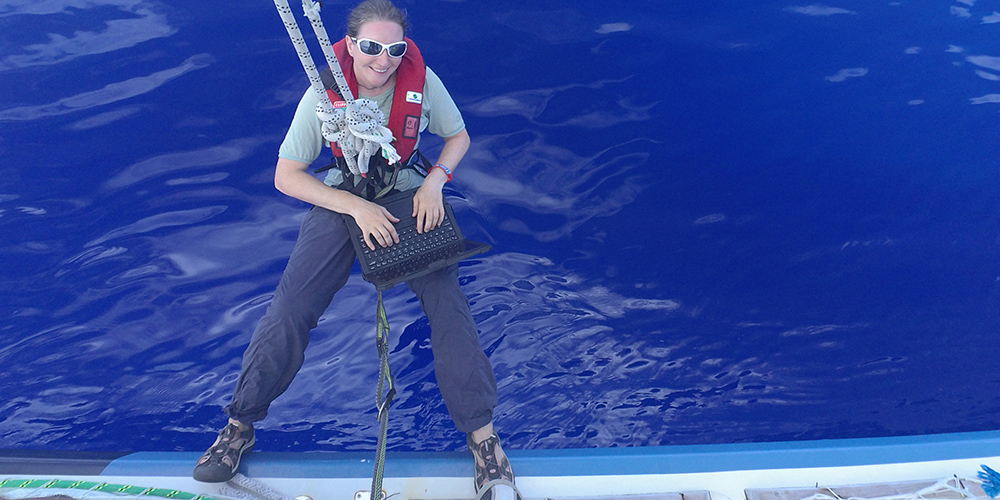 Samantha Harper hangs over the edge of the Dare to Lead clipper ship using a Dell Latitude Rugged laptop