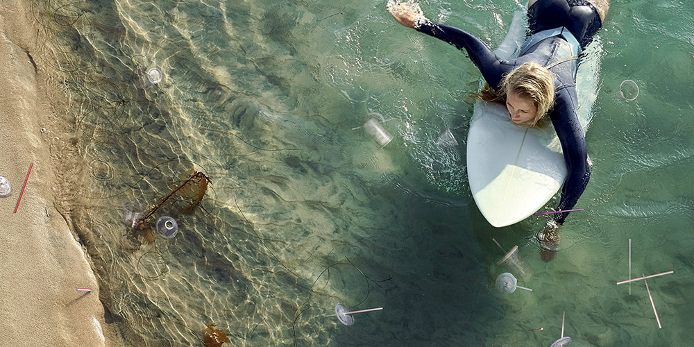 female surfer paddles through plastic cups and straws floating in the ocean