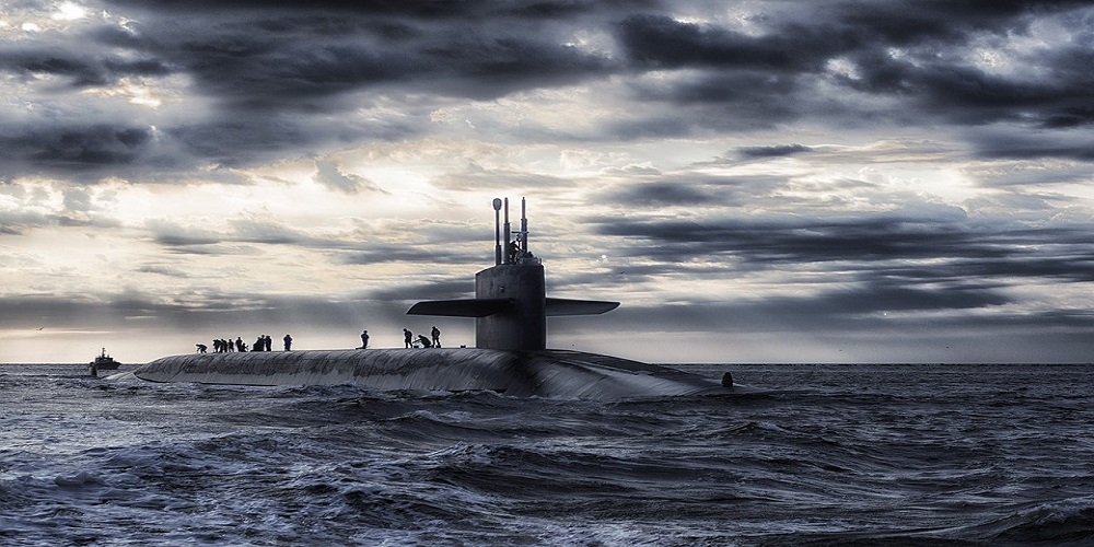 several people stand atop a submarine that has surfaced at sea