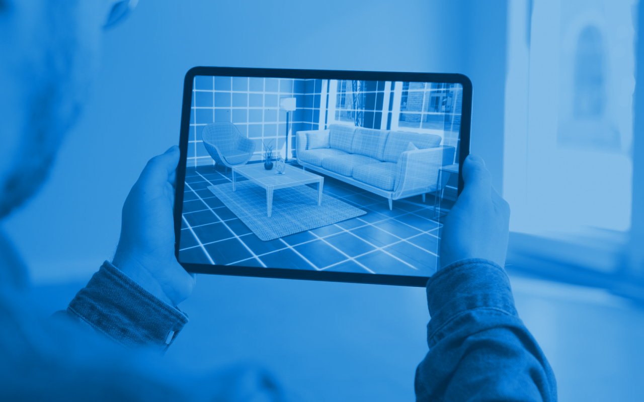 Person holding a tablet with an image of a living room with sofa and coffee table. Image is tinted in blue.