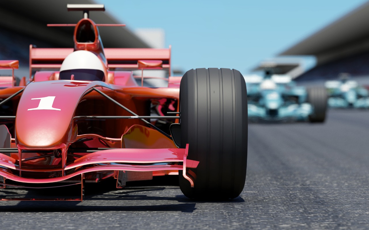 A red Formula 1 race car on the race track with a blue race car in the background,