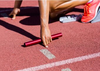 Female runner with baton in left hand takes her position in the starting blocks.