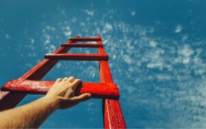 Red ladder rising up to blue sky, representing career growth opportunities.