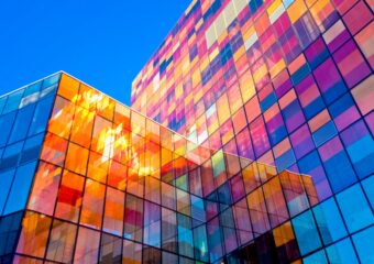 Office building with sunlight reflecting different colors off exterior glass.