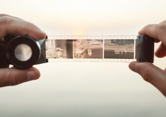 Person holding 35 mm camera film negatives and viewing images with negative viewer lens.