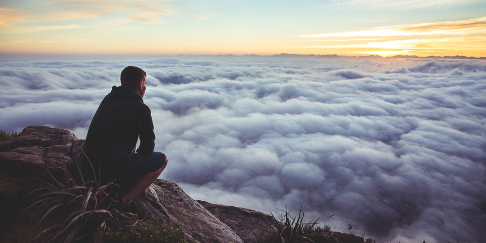 man on mountain above clouds watches sunrise