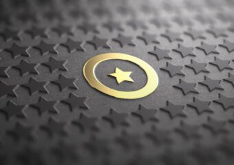Gold star within a gold circle that stands out against a dark background with smaller star shapes.