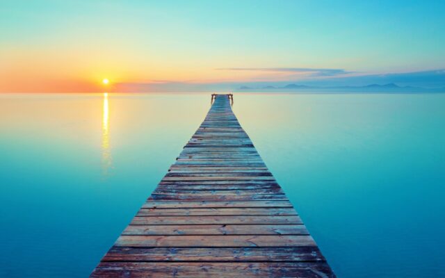 A wooden pier extends over calm water with a sunset in the background.