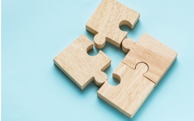 Four wooden puzzle pieces come together to form a square on a light blue background.