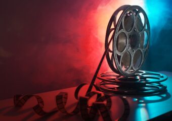 Movie reels with film on a desk with red and blue lighting behind it.