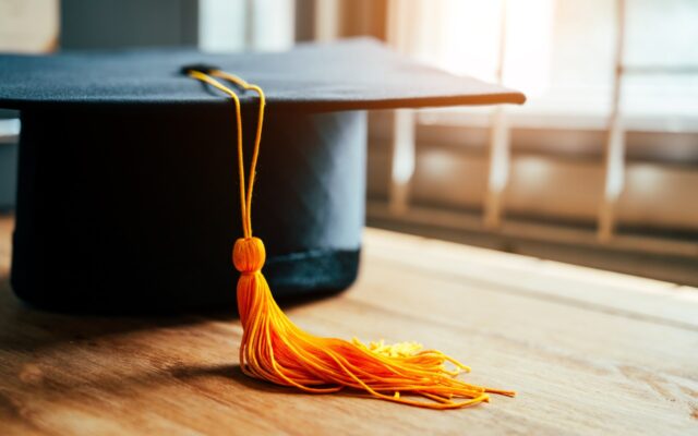 Black graduation cap with yellow tassel on wooden table.