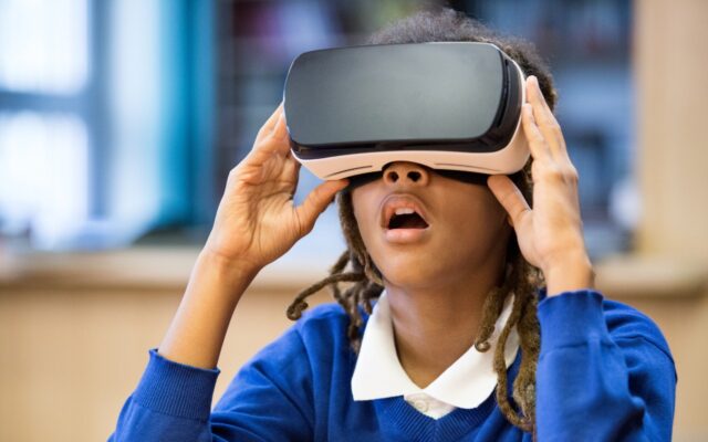 A young African-American girl is using virtual reality goggles.