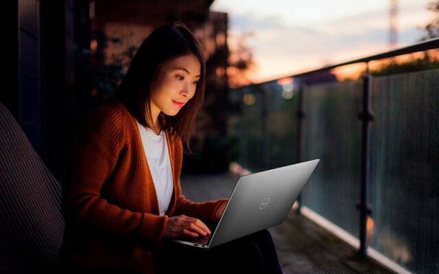 Woman sits outside at sunset working on an XPS laptop.