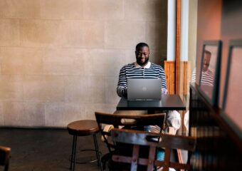African-American man working at a small table in an open space, using his Dell notebook for work.