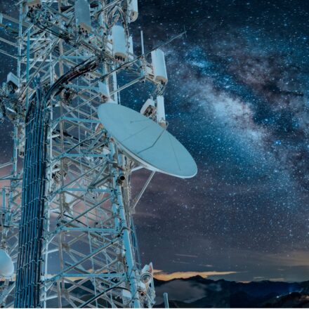 5G communications tower in the left foreground with the Milky Way appearing in the night sky behind it.