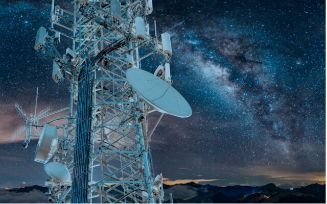 5G communications tower in the left foreground with the Milky Way appearing in the night sky behind it.