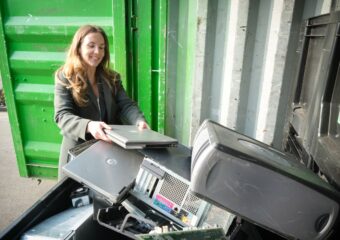 Young woman at an electronics / e-waste collection site, adding an old laptop for recycling.