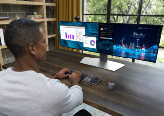 African-American man working from home using dual monitors and wireless mouse and keyboard. Photo taken from over his right shoulder towards the monitors. PC not pictured.