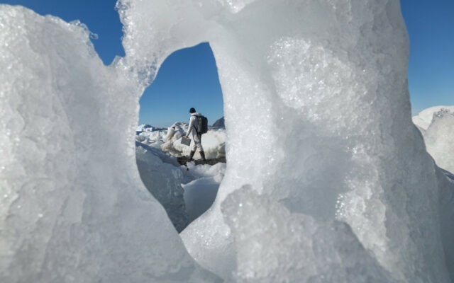 Person in a cold, snowy and icy outdoors environment carries a Dell Rugged Latitude notebook. Image of person taken through a hole in snow and ice formation with a blue sky in the background.
