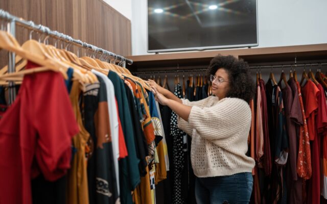 An African-American woman is looking through a rack of clothes in a retail store.