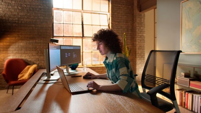 Person in green and white checkered shirt works remotely using a Dell Precision 5000 series model laptop and dual monitors.