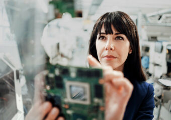 Woman holding up circuit board component in innovation development facility.