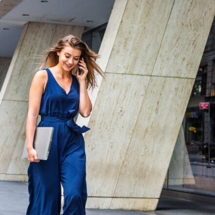 Young businesswoman speaks on the phone, as she walks outside ,while carrying a Dell Latitude 5520 laptop.