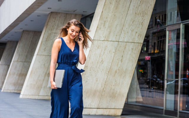 Young businesswoman speaks on the phone, as she walks outside ,while carrying a Dell Latitude 5520 laptop.