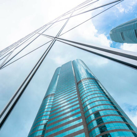Low angle photograph of skyscrapers, with blue sky, other skyscrapers, and clouds reflect off the glass.