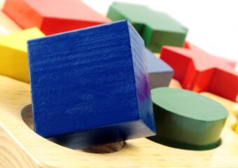 Blue, green, red, and yellow blocks of different shapes on a wodden toy surface with corresponding shaped holes.