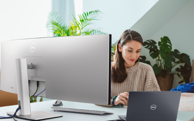 Woman working remotely using a Dell UltraSharp 49 Curved USB-C Hub Monitor and a Dell Latitude 5000 series model laptop.