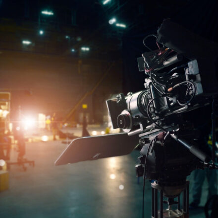 Movie camera on set in a studio as production tasks are happening in the background.