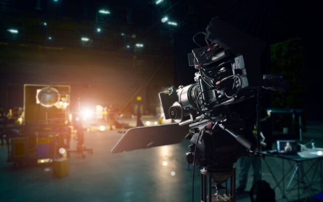 Movie camera on set in a studio as production tasks are happening in the background.