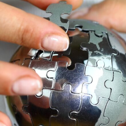 Close up image of a person holding a three dimensional puzzle of Earth in silver, putting in a piece.