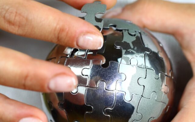 Close up image of a person holding a three dimensional puzzle of Earth in silver, putting in a piece.